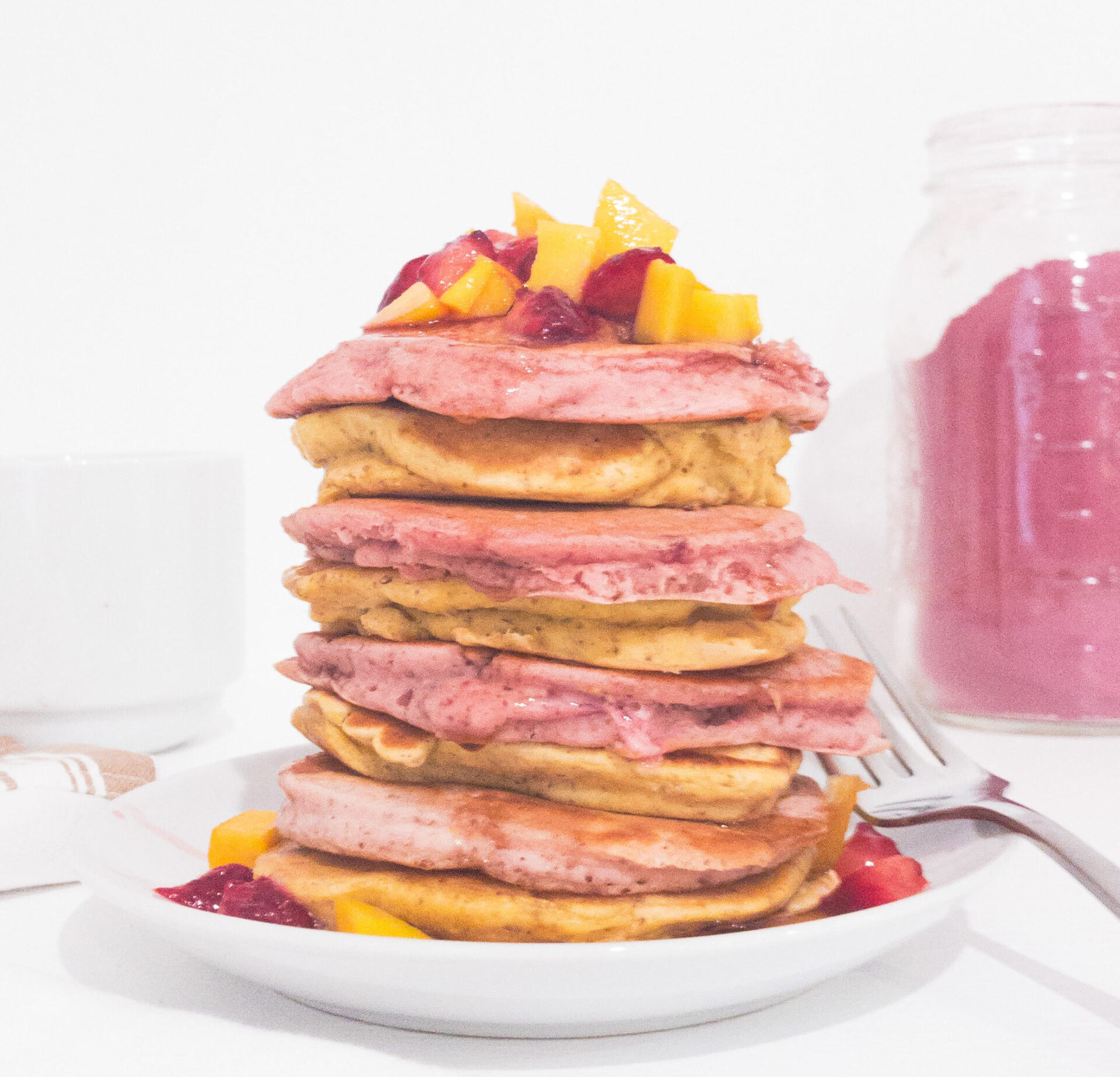 Pink and yellow pancake stack with mangoes and strawberries on top