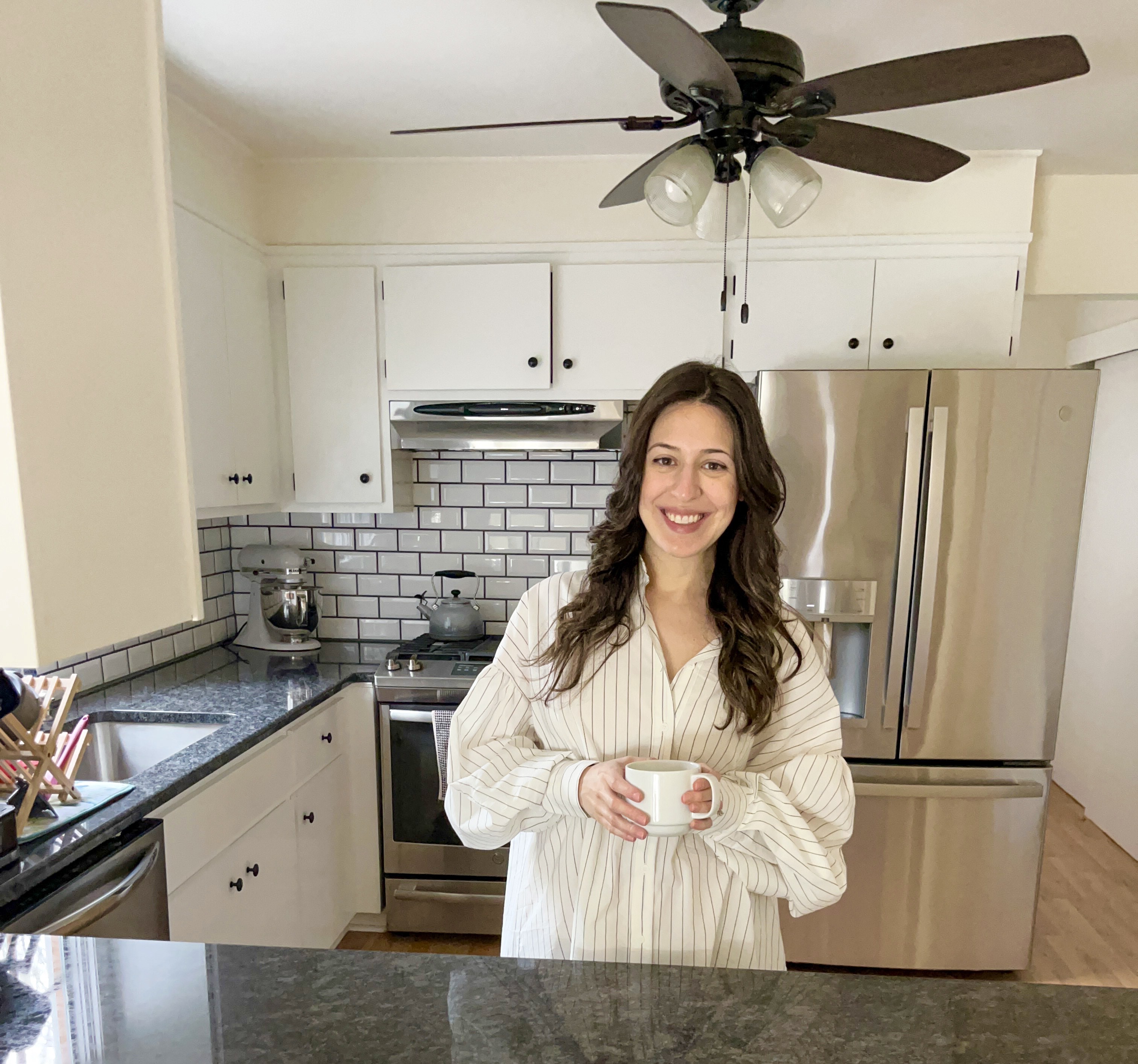 Woman in white dress standing in kitchen smiling with cup of coffee