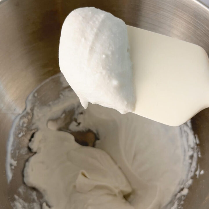 White spatula holding up a dollop of coconut whipped cream over a bowl