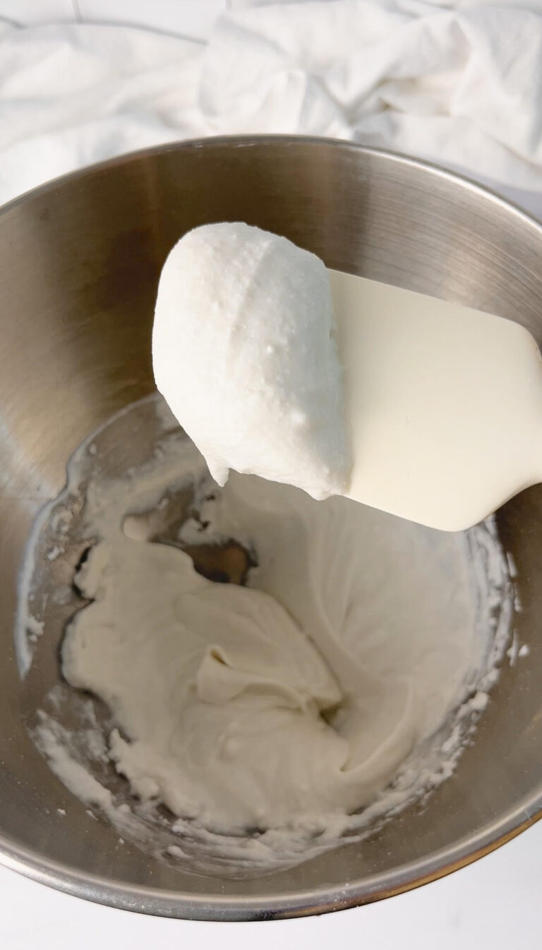 White spatula holding up a dollop of coconut whipped cream over a bowl