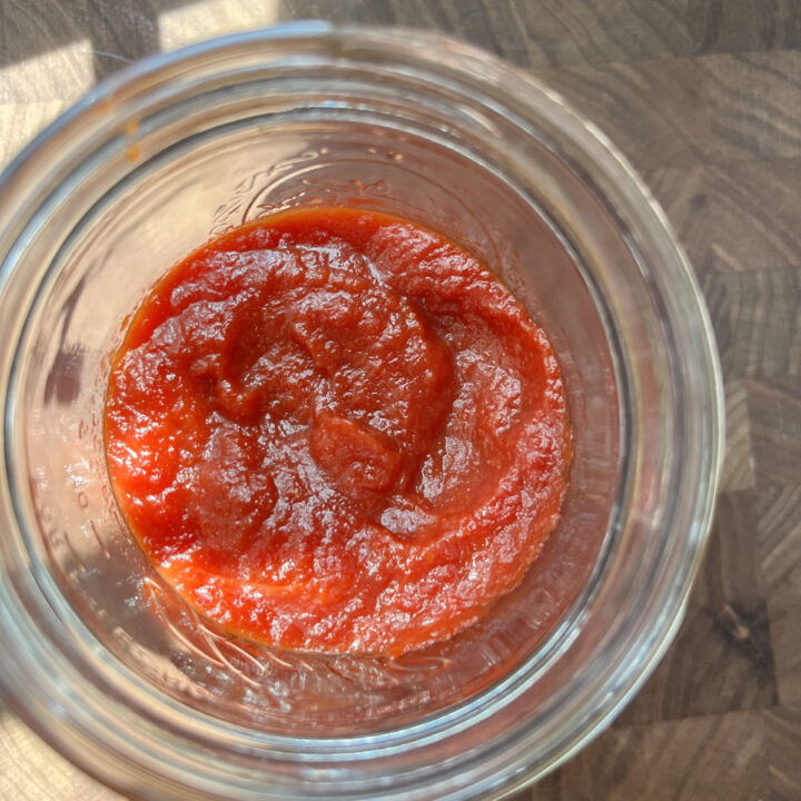 Homemade ketchup in a mason jar on a wooden cutting board