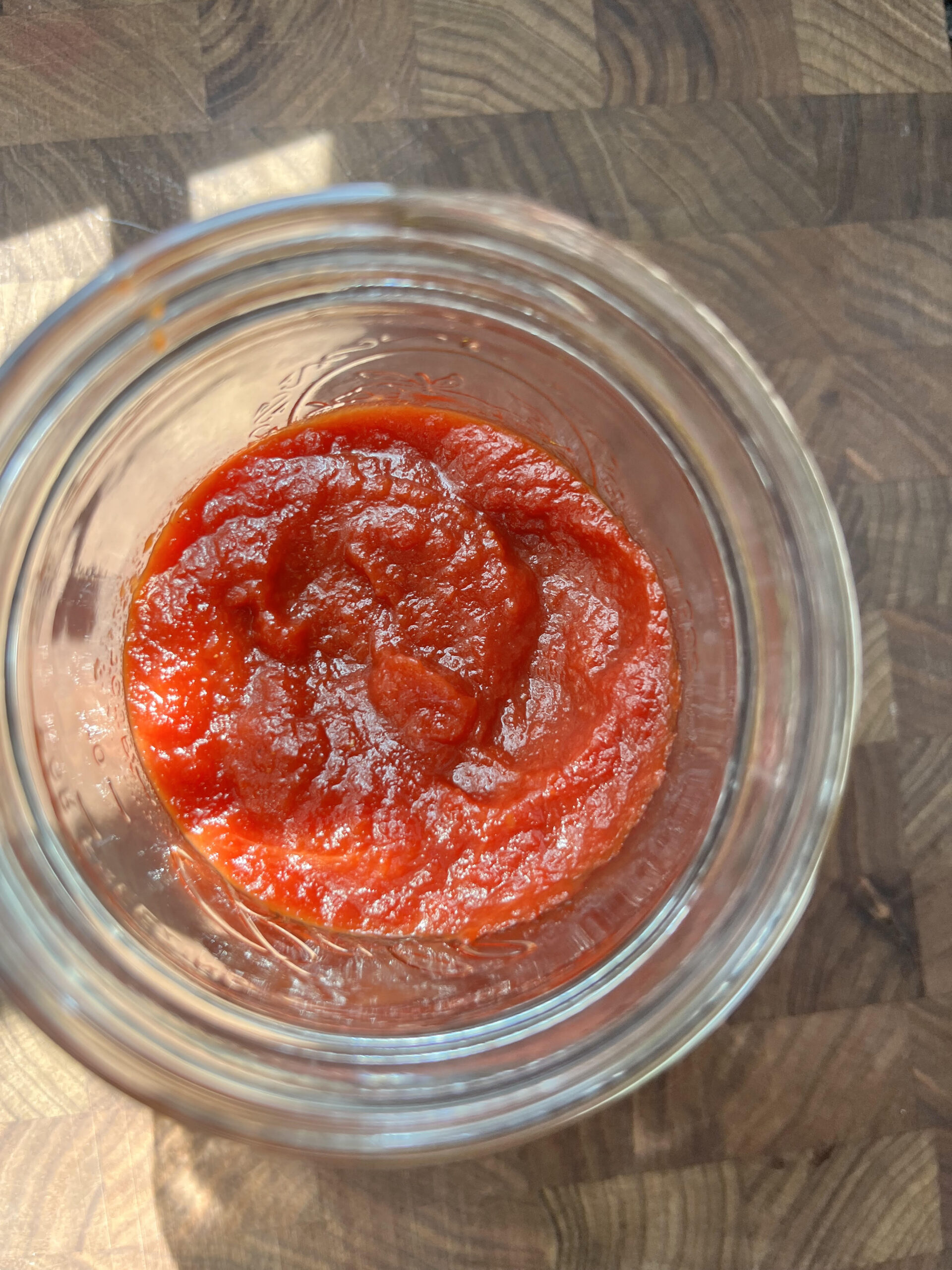 Homemade ketchup in a mason jar on a wooden cutting board