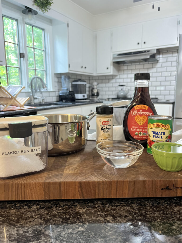 Ingredients for homemade ketchup on a wooden cutting board with a white kitchen in the background