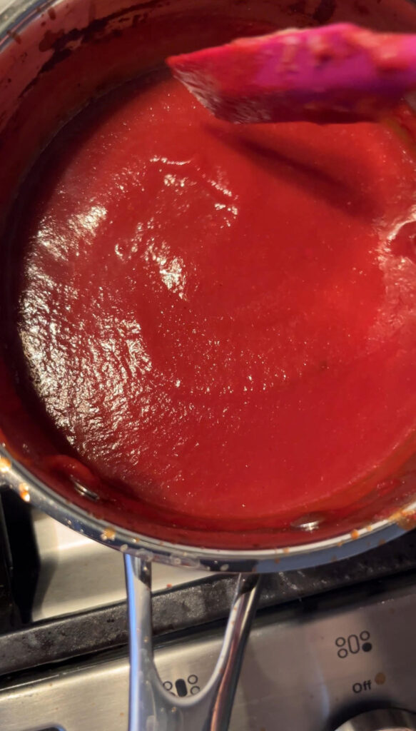 Bright red ketchup cooking in a stainless steel pot on the stove