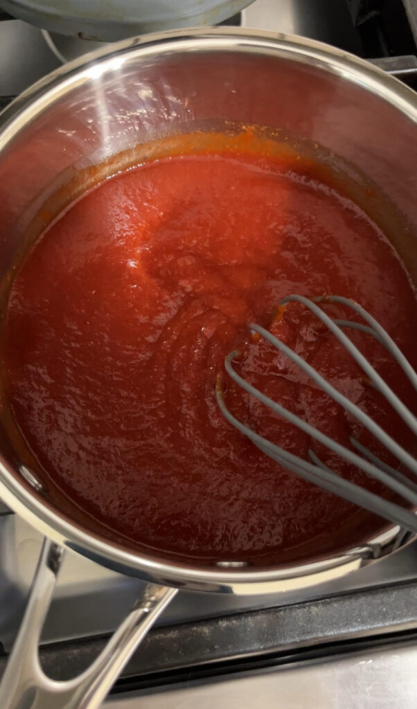 Homemade ketchup cooking on a stove with a whisk in the sauce