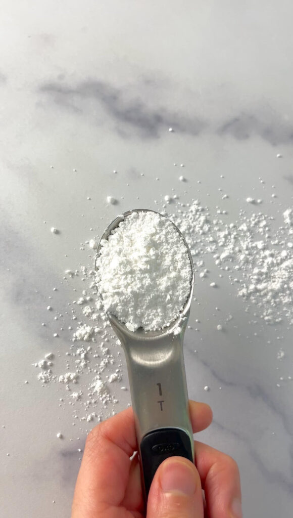 Hand holding a tablespoon of organic powdered sugar over a white countertop